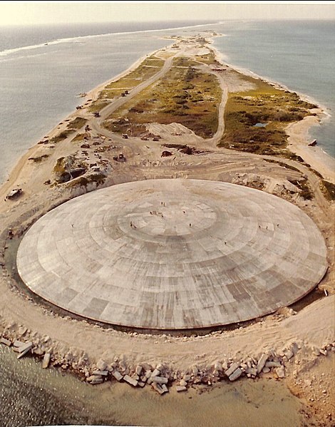 Cactus Dome, île Runit, atoll d'Enewetak. Vue aérienne. En 1977-1980 le cratère créé par le test nucléaire américain Cactus de l'opération Hardtack I a été utilisé pour enfouir 84.000 mètres cubes de sol radioactif provenant des îles contaminés de l'atoll. Le Cactus Dome est un dôme de béton recouvrant les déchets.  (Image : Wikipeadia - US Defense Special Weapons Agency) 